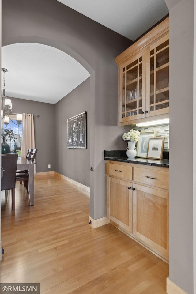 hallway with baseboards, light wood finished floors, arched walkways, and a chandelier