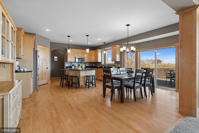 dining room with a chandelier, arched walkways, light wood finished floors, and a healthy amount of sunlight