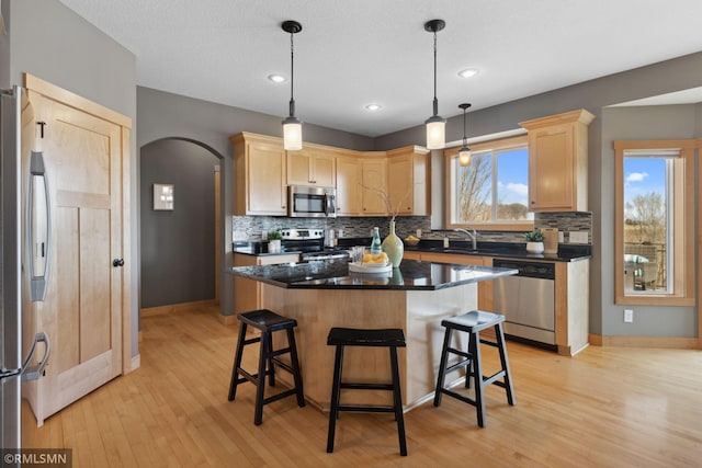 kitchen featuring light wood-style flooring, tasteful backsplash, arched walkways, light brown cabinetry, and appliances with stainless steel finishes