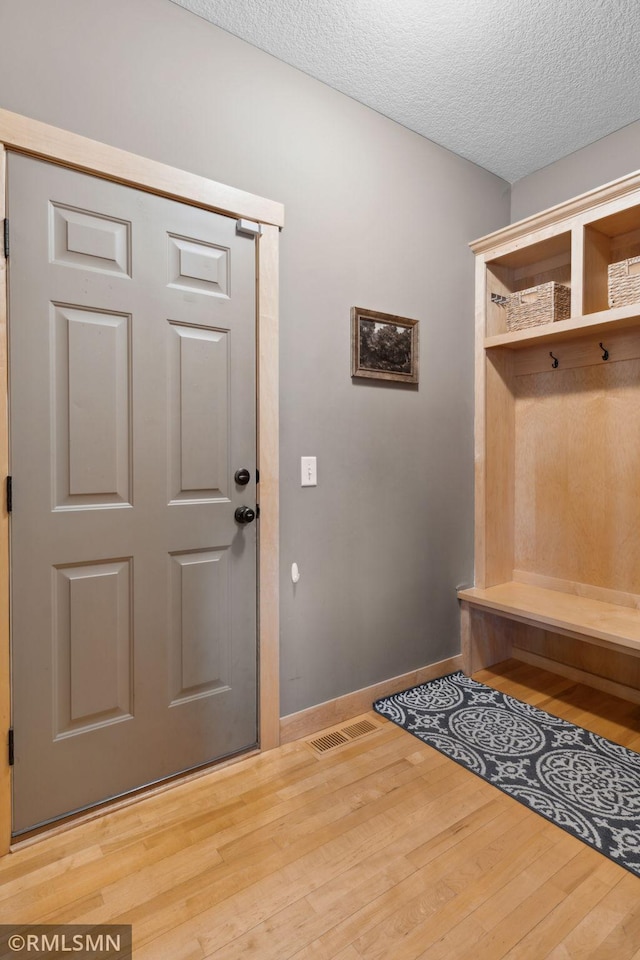 mudroom featuring visible vents, baseboards, wood finished floors, and a textured ceiling