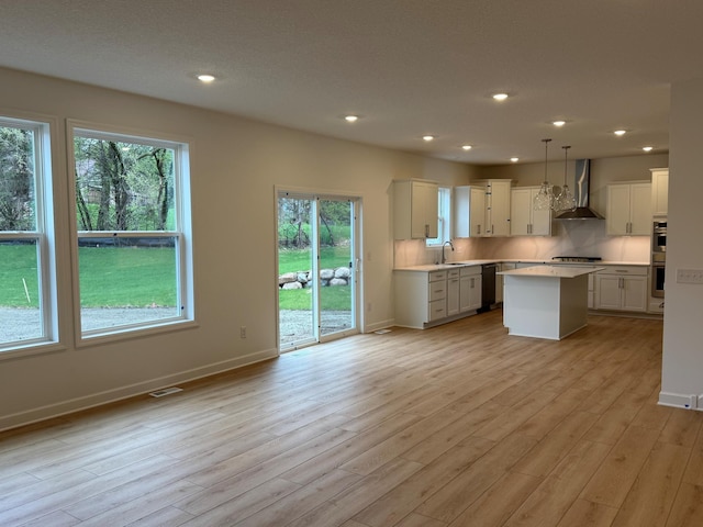 kitchen featuring wall chimney exhaust hood, a sink, black dishwasher, light countertops, and stainless steel double oven