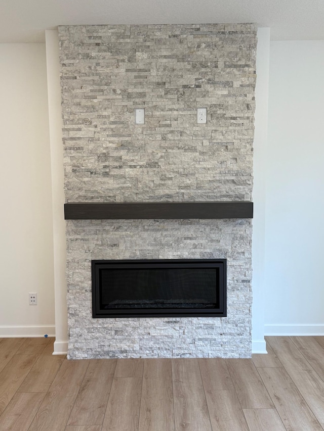 detailed view of a fireplace, wood finished floors, and baseboards