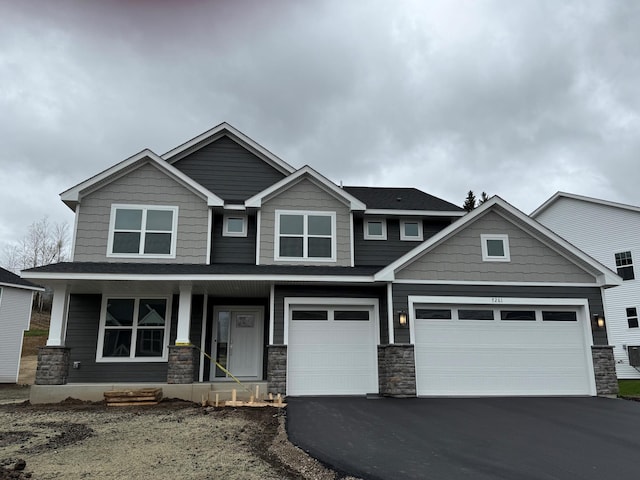 craftsman-style home with stone siding, covered porch, and driveway