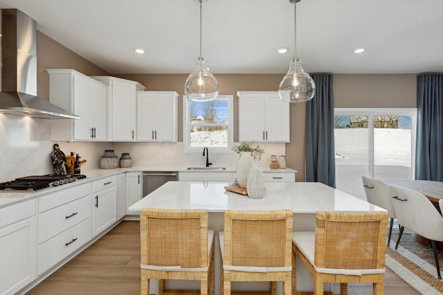 kitchen with wall chimney exhaust hood, a sink, appliances with stainless steel finishes, light wood-type flooring, and light countertops