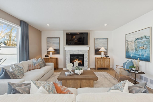 living area featuring a stone fireplace, wood finished floors, recessed lighting, and baseboards
