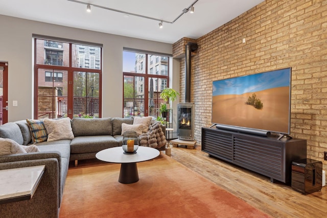 living area featuring a wood stove, wood finished floors, rail lighting, and brick wall