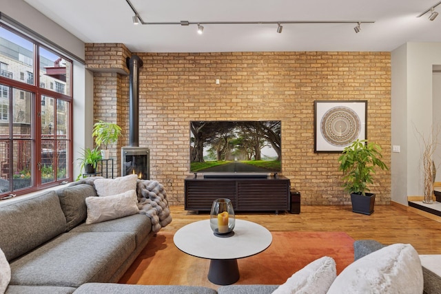 living area with track lighting, a wood stove, wood finished floors, and brick wall