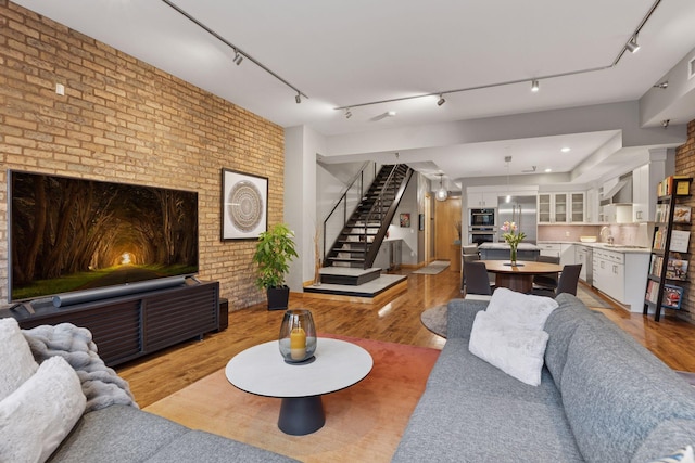 living room with brick wall, stairway, track lighting, and light wood-type flooring