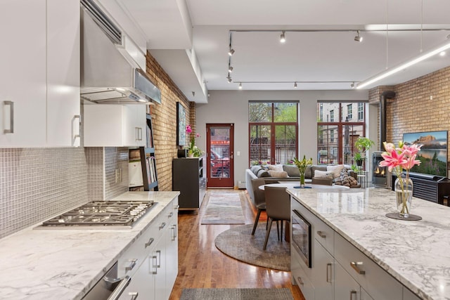 kitchen featuring appliances with stainless steel finishes, wood finished floors, range hood, open floor plan, and light stone counters