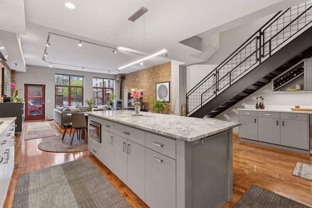 kitchen with gray cabinetry, light wood-type flooring, a kitchen island, brick wall, and open floor plan
