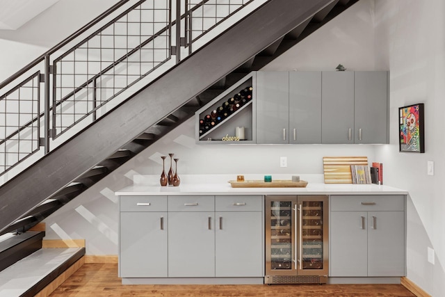 indoor dry bar featuring beverage cooler, stairs, and light wood finished floors