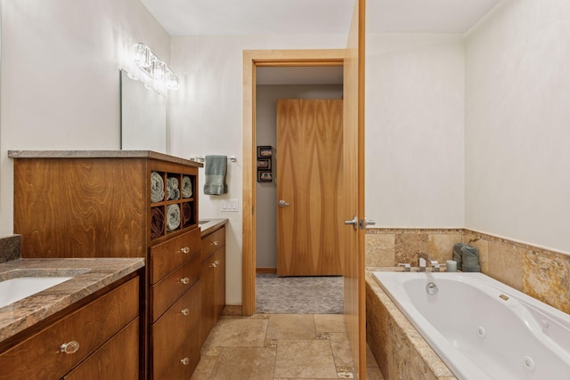 full bath featuring vanity, a whirlpool tub, stone finish floors, and baseboards