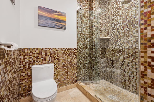 bathroom with tile walls, a tile shower, toilet, a wainscoted wall, and tile patterned floors