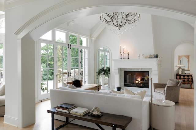 living room featuring a premium fireplace, arched walkways, light wood finished floors, and an inviting chandelier