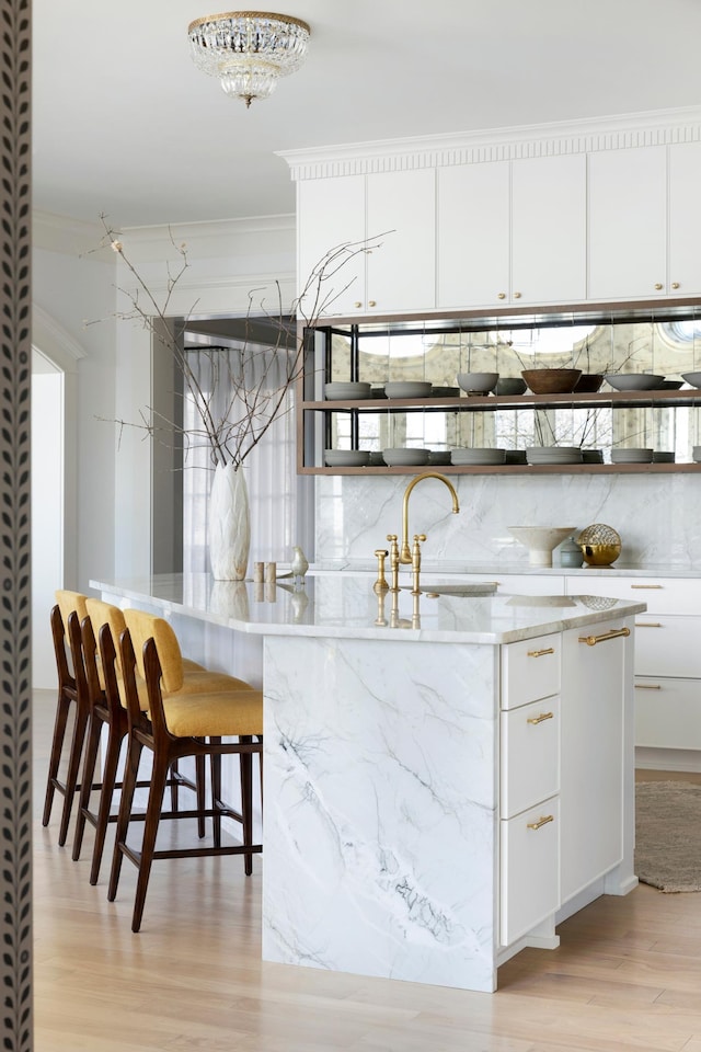 kitchen with white cabinets, a sink, ornamental molding, light wood finished floors, and light stone counters