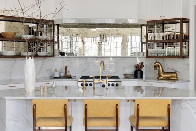 kitchen with light stone countertops, stainless steel gas stovetop, white cabinetry, and backsplash
