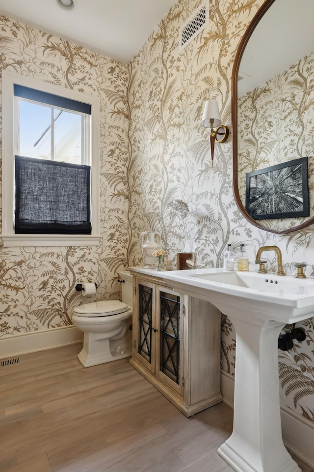 half bath featuring visible vents, toilet, wood finished floors, wallpapered walls, and baseboards