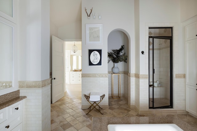 hall with tile walls, arched walkways, wainscoting, and a towering ceiling