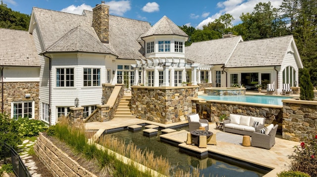 rear view of house with a chimney, an outdoor living space, an in ground hot tub, stairs, and a patio area