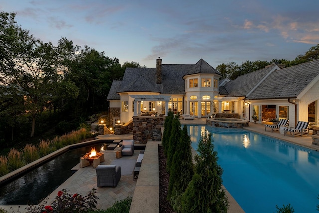 pool at dusk with a patio area, a pool with connected hot tub, and a fire pit