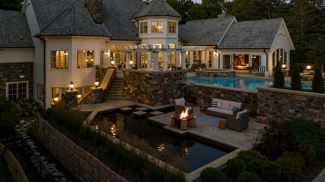 back of house featuring a chimney, an in ground hot tub, an outdoor pool, an outdoor living space with a fire pit, and a patio area