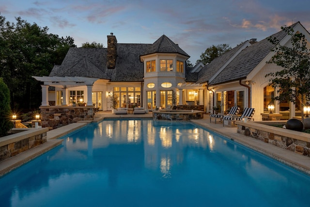 back of house at dusk featuring an outdoor living space with a fire pit, french doors, an outdoor kitchen, and a chimney