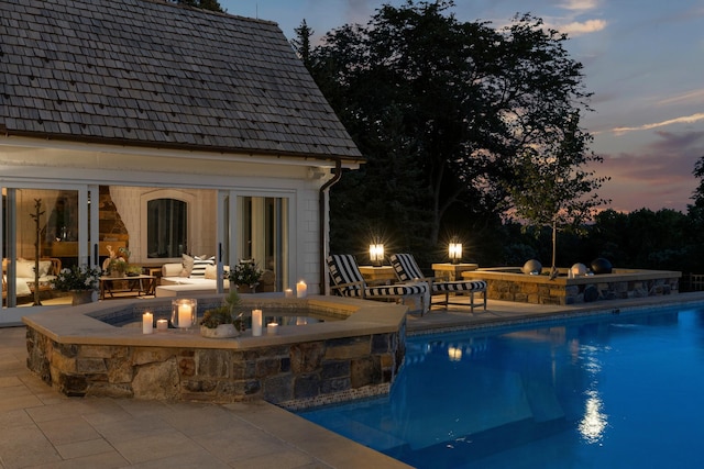 pool at dusk featuring a patio and a pool with connected hot tub