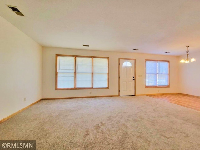 unfurnished living room featuring an inviting chandelier, baseboards, carpet, and visible vents