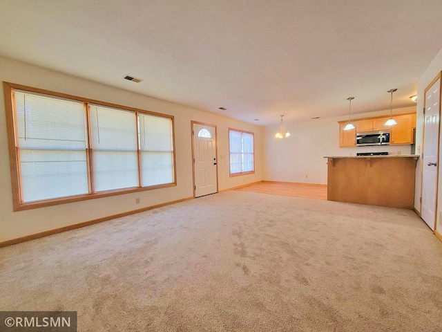 unfurnished living room featuring a chandelier, light carpet, baseboards, and visible vents