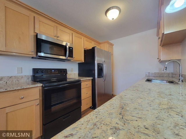 kitchen with a sink, light brown cabinetry, light stone counters, and stainless steel appliances