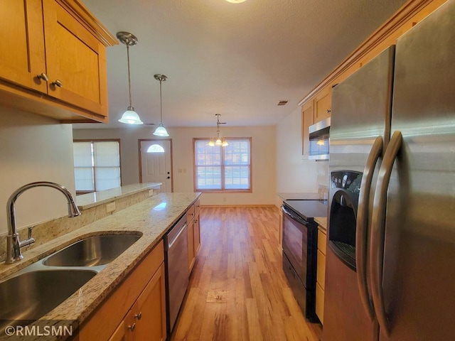 kitchen featuring decorative light fixtures, brown cabinetry, stainless steel appliances, light wood finished floors, and a sink