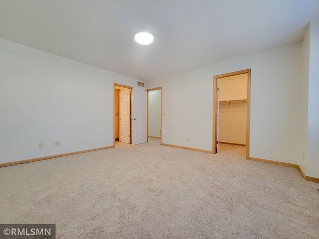 unfurnished bedroom with a closet, baseboards, a walk in closet, visible vents, and light colored carpet