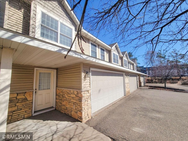 view of home's exterior with a garage, stone siding, and driveway