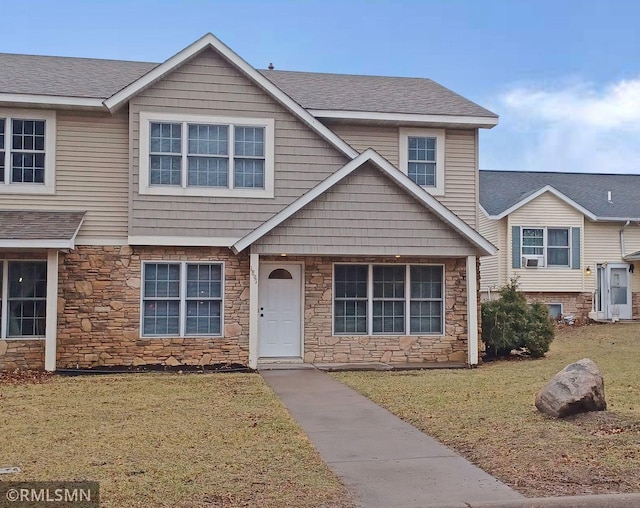 view of front facade featuring a shingled roof, a front yard, and stone siding