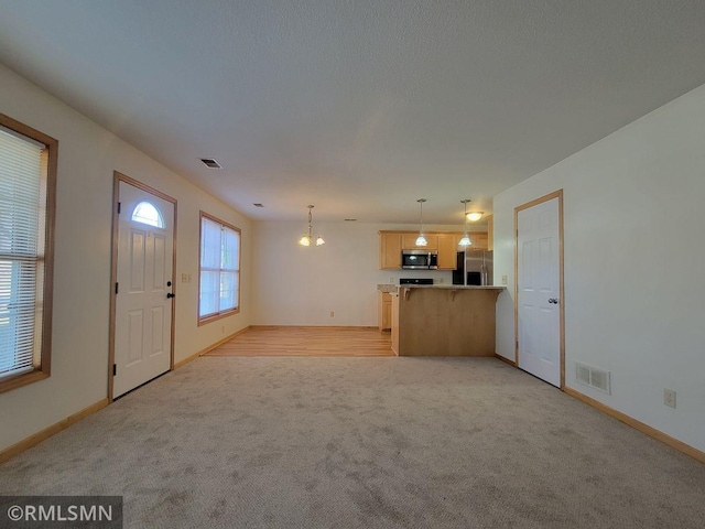 unfurnished living room featuring an inviting chandelier, visible vents, light colored carpet, and baseboards