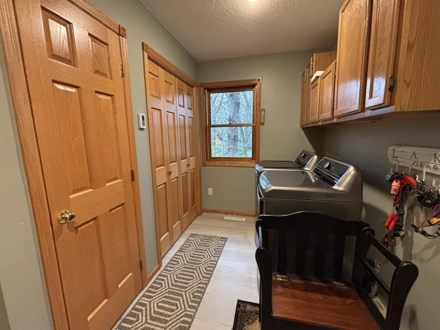 26837 Lake Ethel Rd, Girard Twp, MN 56515 - laundry room featuring independent washer and dryer, cabinet space, a textured ceiling, baseboards, and light wood-style floors