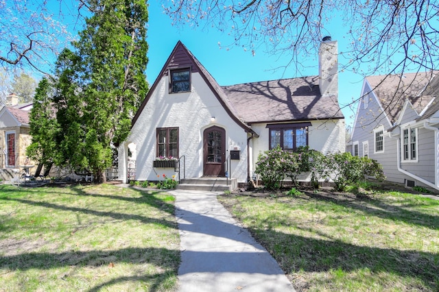 tudor house featuring stucco siding, a chimney, and a front yard