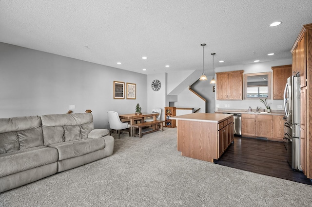 kitchen featuring a center island, a textured ceiling, open floor plan, appliances with stainless steel finishes, and dark colored carpet