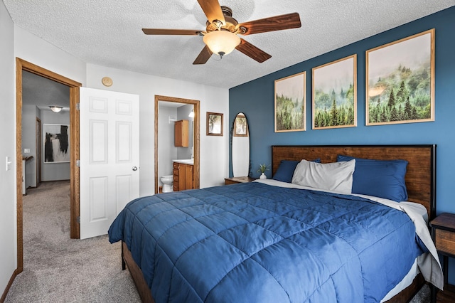 bedroom with ceiling fan, a textured ceiling, light colored carpet, and ensuite bathroom