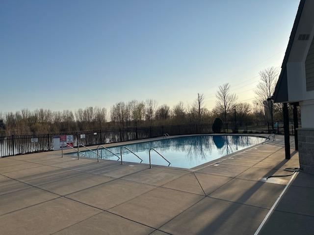 pool at dusk with fence, a community pool, and a patio