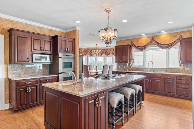 kitchen with an inviting chandelier, a sink, a kitchen island with sink, light wood-style flooring, and stainless steel appliances