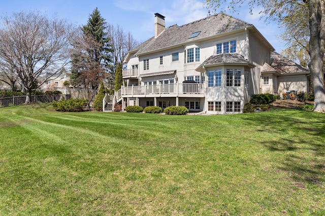 rear view of property with a chimney, a lawn, a deck, fence, and stucco siding