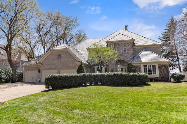 french country inspired facade with driveway, a chimney, brick siding, a front lawn, and an attached garage