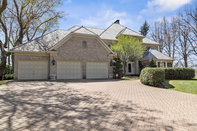 french country home featuring decorative driveway, a garage, and brick siding