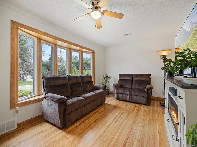1883 County Road C E, Maplewood, MN 55109 - living room featuring light wood finished floors, a textured ceiling, a lit fireplace, and a ceiling fan