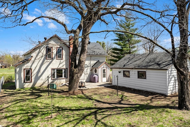 rear view of property with a shingled roof, an outdoor structure, a chimney, and a lawn