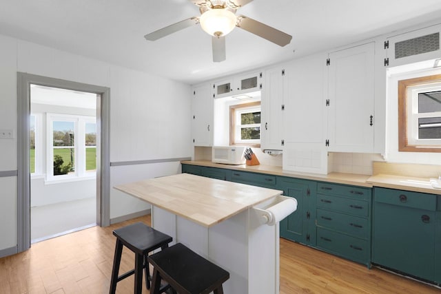 kitchen with light wood-style flooring, a breakfast bar, wood counters, green cabinetry, and white microwave
