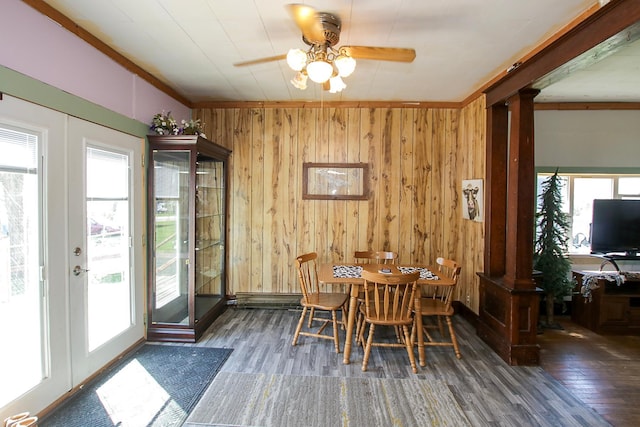 dining room with decorative columns, wooden walls, wood finished floors, and a ceiling fan