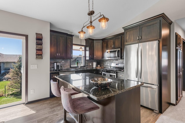 kitchen with dark brown cabinetry, appliances with stainless steel finishes, tasteful backsplash, a sink, and dark stone counters