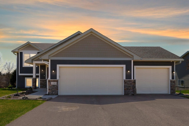 craftsman house with an attached garage, driveway, a shingled roof, and stone siding